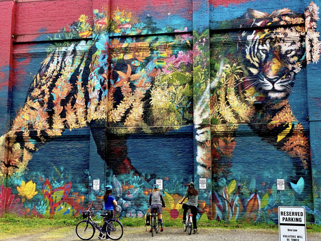 beautiful street art with tiger and flowers with three people on bikes looking at it below