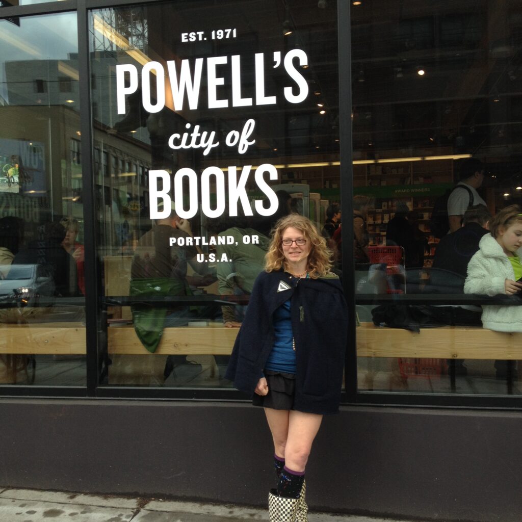 a person in a cape and a short skirt stands in front of a window reading Powells city of books